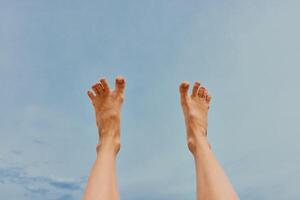 Legs of person raised high in the air against a clear blue sky with a few fluffy clouds in the photo