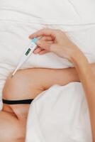Sick woman lying in bed with electronic thermometer in hand and another on chest. concept of illness photo