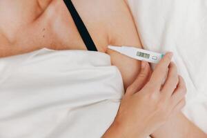 Woman checking temperature in bed with electronic thermometer in mouth. photo