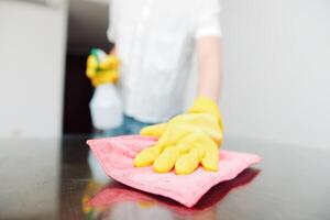Cleaning lady wearing yellow gloves cleaning table with a bottle of cleaning solution on it. photo