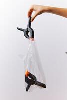 Scissors attached to a plastic bag being held up by a person against a white background. image can photo
