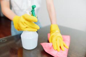Woman cleaning table with yellow gloves using bottle of solution and rag on wooden surface. photo