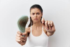 A young woman holding a hairbrush with hair strands caught in it, displaying a worried expression photo