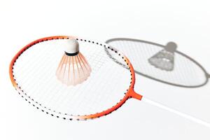 Badminton racket and shuttlecock on white surface with shadow. orange and white colors. photo