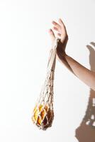 White macrame handbag with orange details held by a hand against a white background. mockup for photo
