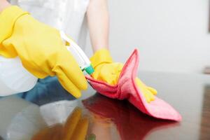 Woman in yellow gloves using cleaning solution and rag to wipe down table. photo