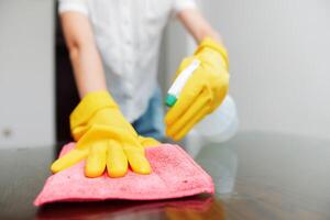Woman wearing yellow gloves cleaning table with sponge and bottle of cleaning solution. photo