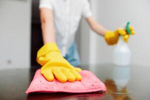 Woman cleaning table with yellow gloves, rag, and cleaning solution bottle. photo