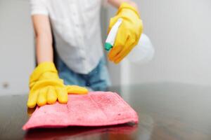 Cleaning woman in yellow gloves wiping table with rag and using solution bottle. photo