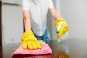Woman cleaning table with sponge and cleaning solution bottle. yellow gloves. photo