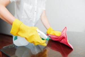 Woman in rubber gloves wipes table with rag and bottle of cleaning solution. photo