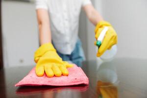 Woman in yellow gloves cleaning table with rag and bottle of cleaning solution. a person is wiping photo