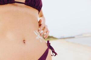 Woman in purple bikini with white sticker on stomach standing on beach with hands on hips. a photo