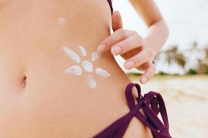 Beautiful woman in bikini applying sun tan lotion on her stomach, with a flower painted on her back photo