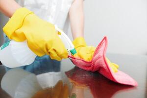 Woman cleaning table with cleaning solution bottle and rag on countertop. yellow gloves on her hands photo