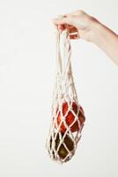 Close up shot of a person holding a white net bag filled with red and green apples on a white photo