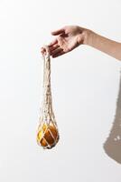 White macrame bag with orange lining held by a person in front of a white wall. hand visible in the photo