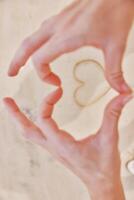 Hands making heart shape with sand on white countertop, holding pair of scissors. photo