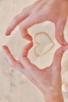 Hands making heart shape with sand on white countertop with ocean view through window. photo