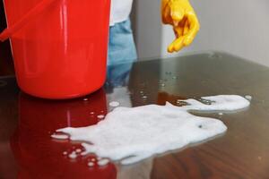 Woman cleaning table with soapy water bucket and red bucket nearby. a woman is cleaning a table with photo