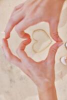 Hands forming heart in sand with feet on ground. romantic gesture on beach. love and connection photo