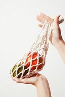 Person holding a white net bag filled with fresh green and red apples against a white background photo