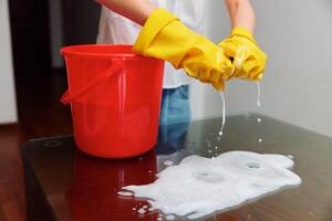 Woman cleaning with bucket of soapy water and red bucket on table. photo