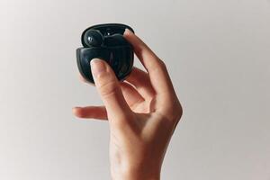 Earbud and small black device held by a person against a white background. photo