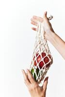 Person holding a white net bag filled with green and red apples on a white background. photo