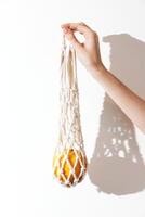 Macrame bag in white color being held by a person's hand, with an orange accent and a shadow cast on photo