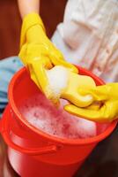 Cleaning woman in yellow gloves wiping red bucket with sponge on top. photo