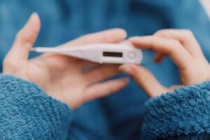 Person holding electronic thermometer in hand wearing blue sweater in front of face. photo