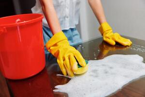 Woman cleaning table with soapy water and red bucket wearing yellow rubber gloves. photo