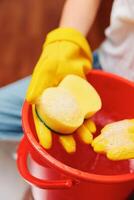 Woman with yellow rubber gloves holding sponge in red bucket filled with soap and water. cleaning photo