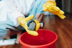 Person wearing rubber gloves holding a rock in a bucket, with a red bucket nearby, on a wooden floor photo
