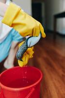 Person wearing rubber gloves is cleaning a red bucket with a sponge. photo