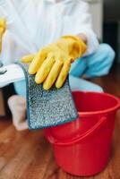 Person cleaning floor with sponge and bucket of water while wearing yellow gloves. photo
