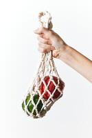 Hand holding white net bag with red and green peppers on white background. photo