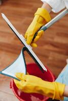 Cleaning person in yellow gloves mopping the floor in front of a red bucket with a cloth. photo