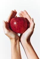 Hands holding a ripe red apple against a plain white background. a simple and natural image of photo