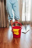 Cleaner with mop and bucket standing on wooden floor in front of window in room. photo