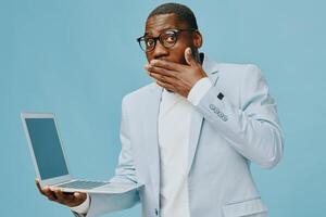 A surprised model holding a laptop with a shocked expression against a blue background The photo
