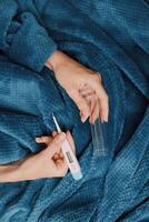 Person holding a thermometer while laying on a blue blanket with another thermometer in hand. photo