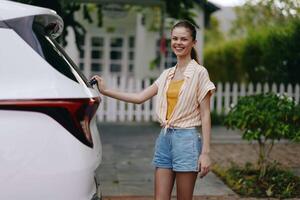 A cheerful young woman with a joyful expression opens the trunk of her car parked in an outdoor photo