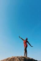 A swimmer in a red swimsuit poses gracefully on a rock, with a bright blue sky in the background photo