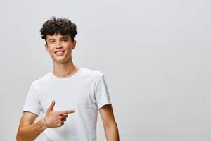 A cheerful young man with curly hair gesturing with his right hand, pointing to the side while photo