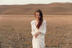 Woman standing in white dress in open field with mountains in background on travel beauty and photo
