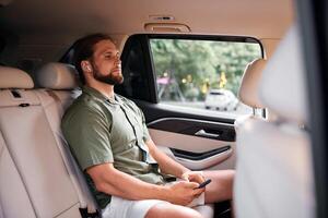 A man in a light green shirt and white shorts sits calmly in a car s backseat, wearing wireless photo