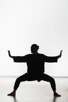 Silhouette of a person practicing qigong energy exercises on a light background photo
