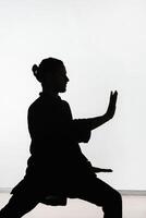 Silhouette of a person practicing qigong energy exercises on a light background photo